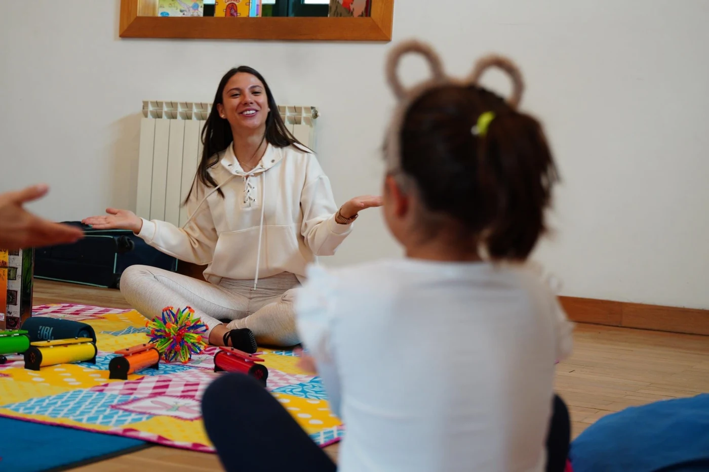Carla Moreira interage com uma criança durante uma sessão, com instrumentos musicais sobre o tapete